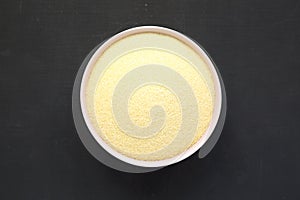 Dry semolina durum flour in a pink bowl over black surface, top view. Overhead, from above, flat lay