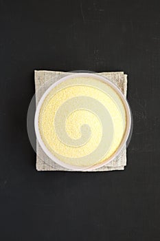Dry semolina durum flour in a pink bowl over black surface, top view. Overhead, from above, flat lay. Close-up