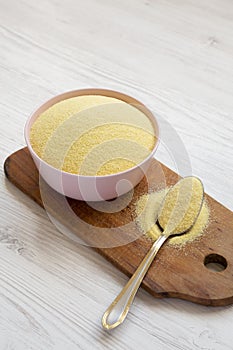 Dry semolina durum flour in a pink bowl over white wooden background, side view