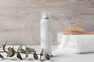 Dry shampoo spray, towel and eucalyptus on white wooden table