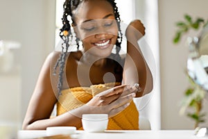 Dry skin treatment. Happy black lady in towel applying moisturising soothing cream at elbow zone at home, selective