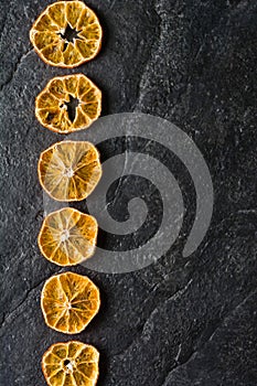 Dry slices of citrus fruits on a black slate background.