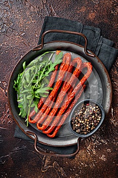 Dry smoked Kabanos or cabanossi traditional Polish thin sausages on a steel tray. Dark background. Top view