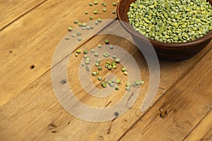 Dry split peas. Brown clay bowl. A scattering of green pea beans against a wooden background. Uncooked food. Healthy food. Close-