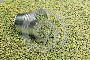 Dry split peas and a metal bucket. The tipped small bucket lies on top of the green uncooked beans. View from above at an angle.