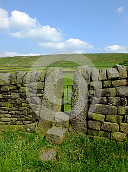 A dry stone wall with stone stile or narrow gate with steps in a yorkshire dales hillside meadow with a bright blue summer sky