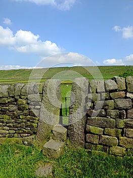 A dry stone wall with stone stile or narrow gate with steps in a yorkshire dales hillside meadow with a bright blue summer sky photo