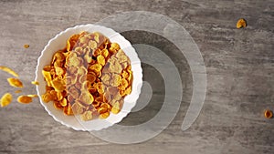 Dry sweet breakfast consisting of yellow cornflakes flying in slowmo from above into a white plate