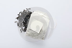 Dry tea leaves and unused bag with tag on white, top view. Space for text