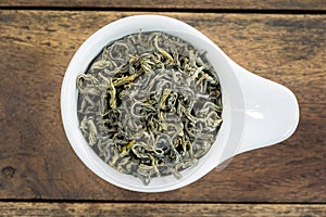Dry tea leaves in a white cup on wood