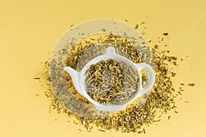 Dry tea from medicinal plants   on a teapot-shaped plate on yellow background