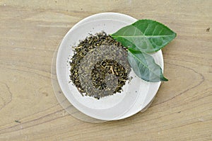 Dry tea in whte plate and fresh leaves on wooden table