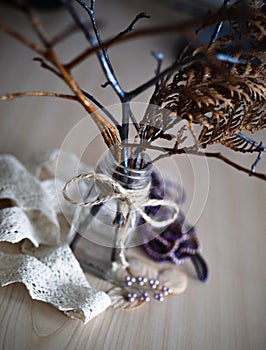 Dry tree branches in a transparent jar with a rope tied in a bow on it standing on wooden surface