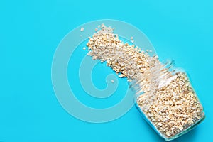 Dry uncooked oats in glass jar spilled on blue background. Digestion immunity boosting food healthy balanced diet