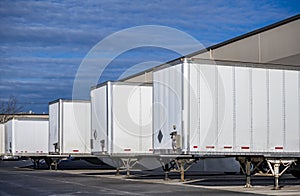 Dry vans semi trailers without of semi trucks standing in row at warehouse dock gates for loading commercial cargo for the next