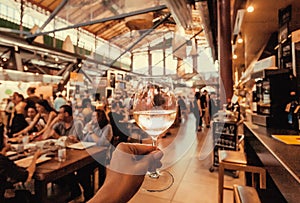 Dry wine in glass of hungry tourist inside crowd food market with fast-food stores and table for eating, Florence, Italy