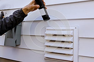 Dryer exhaust fan on side of house with plastic white trim with silicone