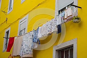 Drying clothes outside windows against yellow wall. Bright colorful building in Portugal. Traditional house exterior in Europe.