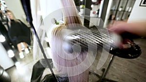 Drying long blonde hair with hair dryer and round brush.