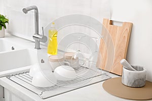 Drying rack with clean dishes near sink in stylish kitchen