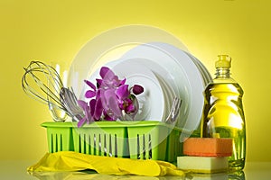 On drying rack clean dishes, utensils, glove, sponge and flowers Orchid on yellow
