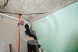 Drywall installation, wall alignment. Laser measurement during renovation. Construction tools and equipment. Red laser