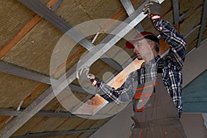 Drywall plaster wall metal fixation. Man holding metal ruler against metal frame on unfinished attic ceiling