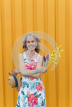 Smiling mature woman with flowers Yellow background