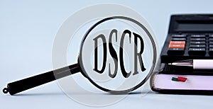 DSCR - acronym on magnifying glass on a light background with calculator, notepad and pen