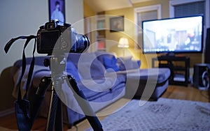 DSLR camera mounted on a tripod capturing a comfortably furnished living room with a blue sofa and television on.