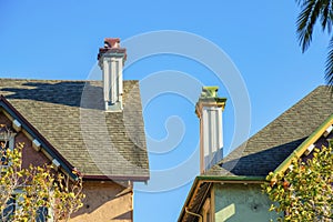 Dual roof chimneys with brown tiles and white decorative chimneys with metal vents and wooden exterior and front yard