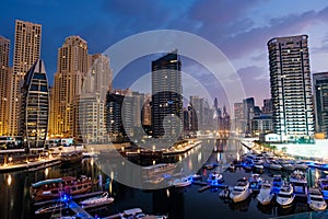 Dubai marina with boats and buildings with gates at night with lights and blue sky