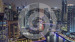 Dubai Marina with several boat and yachts parked in harbor and skyscrapers around canal aerial night timelapse.