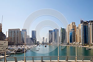 Dubai Marina skyscrapers and boats in harbor in a sunny day, blue sky in Dubai, United Arab Emirates