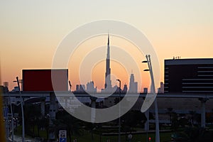 Dubai skyline with Burj Khalifa skyscraper at sunset, clear sky with flyover, billboards in United Arab Emirates