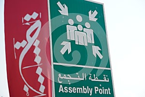 Dubai UAE - November 2019: Emergency assembly point information sign in white paint on green background fixed to a pole to direct