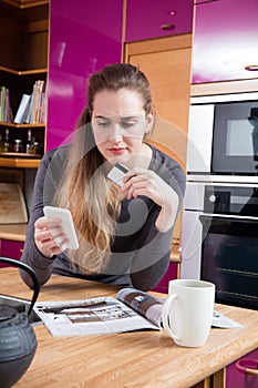 Dubious beautiful young woman shopping online from her home kitchen photo