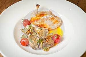 Duck leg with mussels and pickled tomatoes. On a white plate. On a rustic wooden background