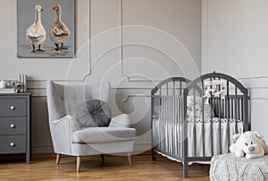 Ducks on cute oil painting in tasteful baby room with grey armchair and wooden crib, copy space on empty wall photo