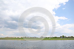 Ducks swimming in lake near village under sky with clouds