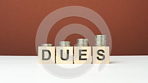 dues text on wooden blocks with coins on brown background