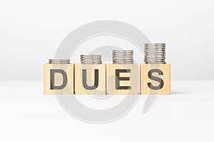 dues text written on wooden block with stacked coins on white background