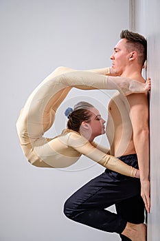 A duet of acrobats showing a pair trick. A woman in gymnastics overalls in a handstand over a shirtless man lies on his