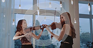 Duet of exciting female violinists performing instrumental music at window