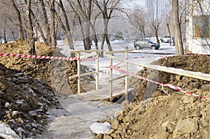 Dug trench with fence tape and wooden bridge above.