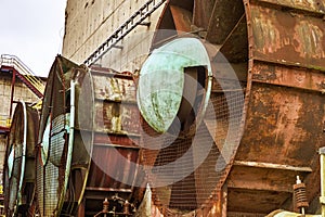 An old, rusty steel fan sits among weathered industrial architecture, a reminder of days gone by