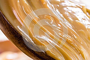 dulce de leche or homemade caramel dripping from wooden spoon, macro photo of food
