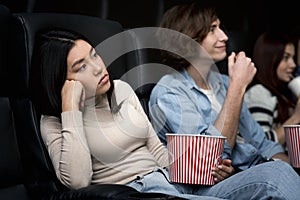 Dull date. Bored young lady with boyfriend watching movie in cinema