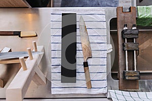 Dull and rustic Japanese kitchen knife waiting for sharpening on blue strip white fabric with sharpening equipment