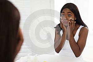 Dull Skin Concept. Confused Black Woman Looking At Mirror And Touching Face